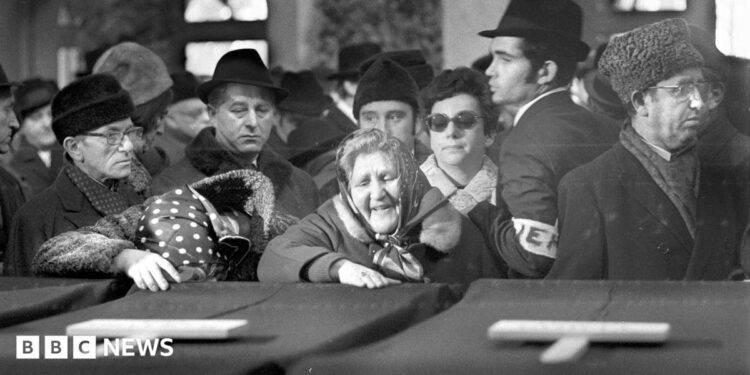 Women mourn the victims in a black and white photo showing coffins