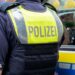 A German police officer standing next to a police vehicle. The officer wears an operational vest that reads "polizei".