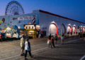People walk along the Ocean City, New Jersey, boardwalk as the Ferris wheel rises in the background