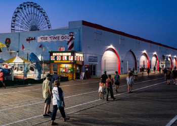 People walk along the Ocean City, New Jersey, boardwalk as the Ferris wheel rises in the background