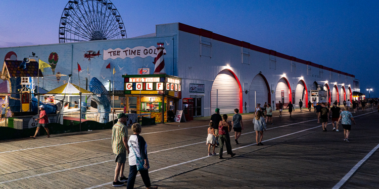 People walk along the Ocean City, New Jersey, boardwalk as the Ferris wheel rises in the background