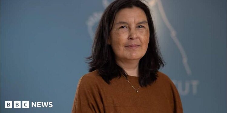 A woman wearing a brown top stands against a blue background