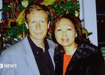 A police handout of Peter Chadwick and his wife Quee Choo Chadwick. They are shoulder to shoulder and looking at the camera, stood in front of a Christmas tree. He is in a grey suit jacket and black shirt, she is wearing a red top and black jacket.