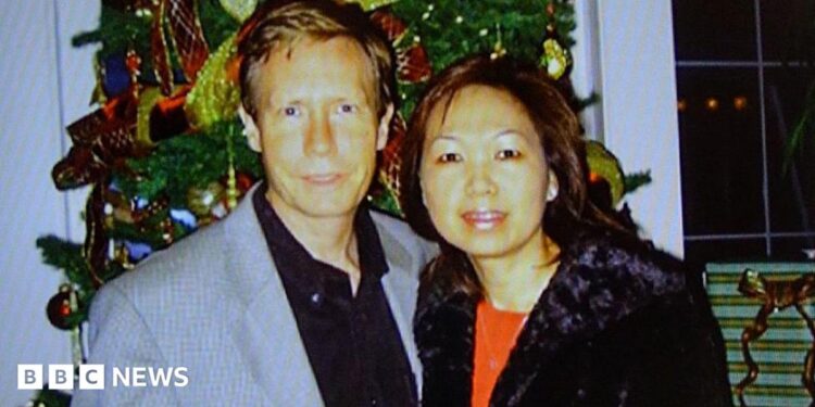 A police handout of Peter Chadwick and his wife Quee Choo Chadwick. They are shoulder to shoulder and looking at the camera, stood in front of a Christmas tree. He is in a grey suit jacket and black shirt, she is wearing a red top and black jacket.