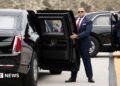 Two US Secret Service agents, both in suits, one in sunglasses, hold open the back passenger doors on two versions of the "Beast" armoured limousine.