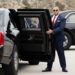 Two US Secret Service agents, both in suits, one in sunglasses, hold open the back passenger doors on two versions of the "Beast" armoured limousine.
