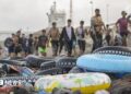 Rubber flotation rings sit on a beach in front of a line of arriving migrants in Ceuta.
