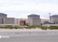A still image of the Gravelines nuclear power plant, with three stone-coloured units connected by a large white wall, set behind a stretch of empty coast with the tide out.