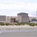 A still image of the Gravelines nuclear power plant, with three stone-coloured units connected by a large white wall, set behind a stretch of empty coast with the tide out.