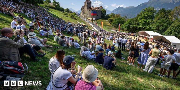 Hundreds of people gather on the slopes below Vaduz Castle, the palace and official residence of the Prince of Liechtenstein, during its National Day celebrations in Vaduz, on 15 August. Mountains can be seen in the background.
