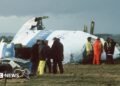 Emergency service workers stand next to the wreckage of Pan Am flight 103 in a field east of Lockerbie.