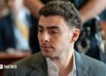 Luigi Mangione is seen from the shoulders up, sitting at the defence table in court. He wears a charcoal grey suit.