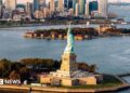 aerial shot of Statue of Liberty and waters surrounding it with New York skyline in background