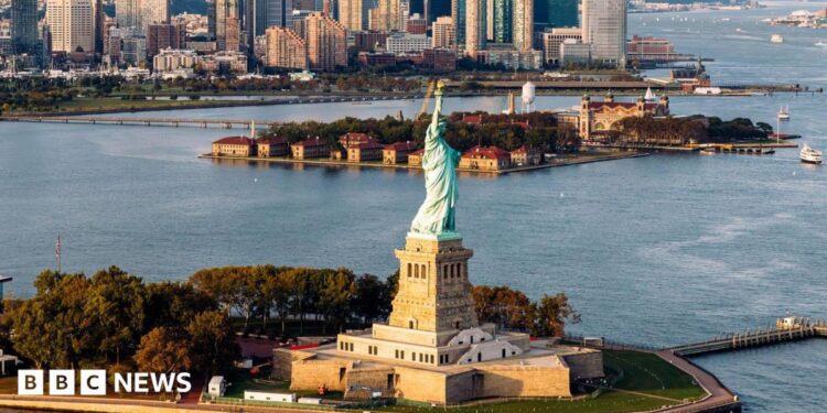 aerial shot of Statue of Liberty and waters surrounding it with New York skyline in background