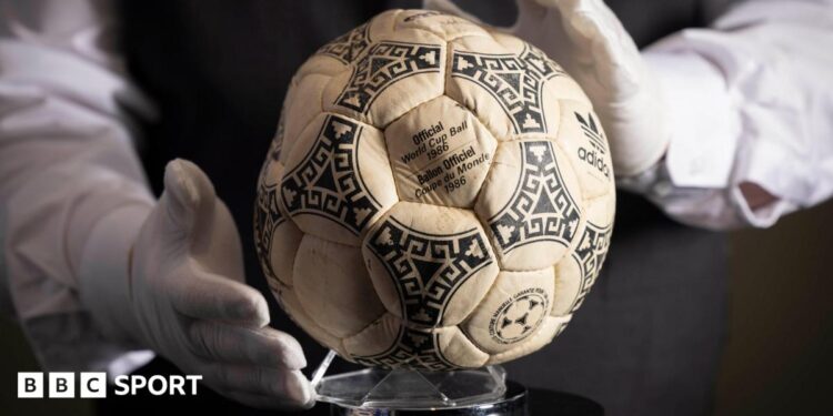 A person wearing white gloves places the football used in the 1986 World Cup quarter-final on a stand