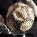 A person wearing white gloves places the football used in the 1986 World Cup quarter-final on a stand