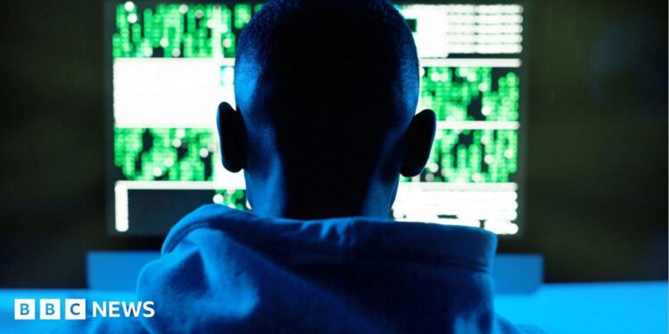 Rear view of a male model in a hoodie in front of a computer in South Africa