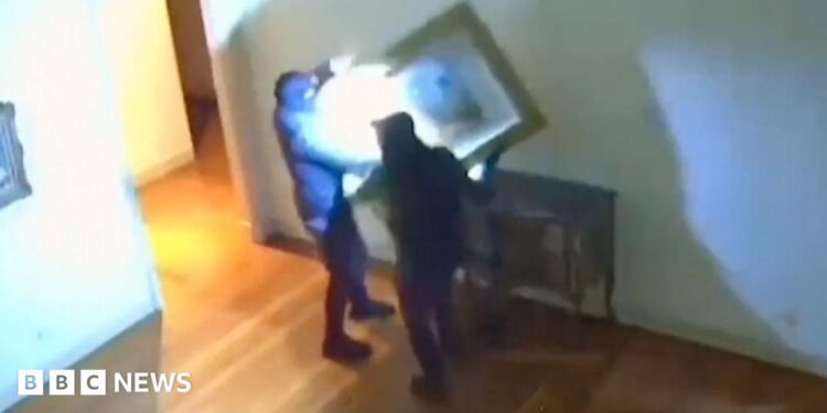 A still from CCTV footage shows two thieves taking artwork off a wall inside a museum in Italy.