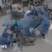 CCTV image of an operating room with doctor falling over and grabbing the operating table