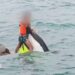 A boy wearing a lifejacket holds on to the top of a capsized jet ski as a man swims next to him in the sea