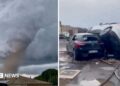 A tornado is seen spinning above a house in the clouds, with two cars on top of each other on the right.