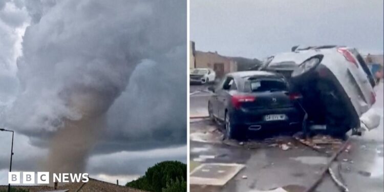 A tornado is seen spinning above a house in the clouds, with two cars on top of each other on the right.