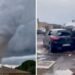 A tornado is seen spinning above a house in the clouds, with two cars on top of each other on the right.