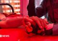Person holds hand of victim on hospital bed