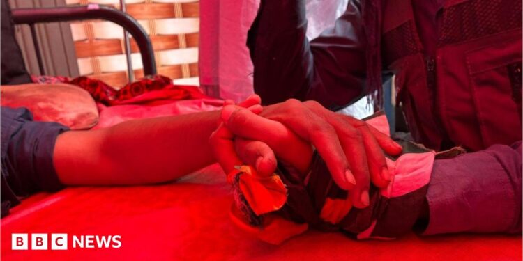 Person holds hand of victim on hospital bed