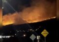 Picture taken at night showing fires burning on hill, plumes of white smoke covering the skies