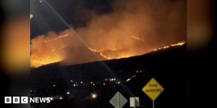 Picture taken at night showing fires burning on hill, plumes of white smoke covering the skies