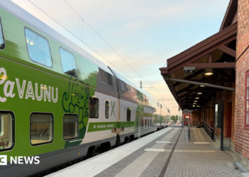 A blue train with Lumo branding travelling under overhead wires.