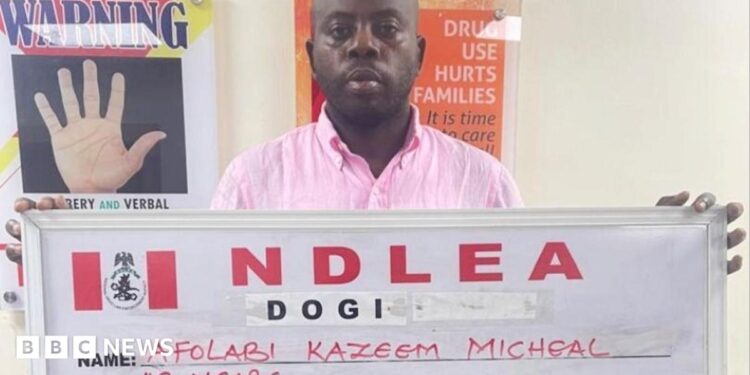 Afolabi Kazeem Micheal holds up a NDLEA sign with his name and age after his arrest in Lagos