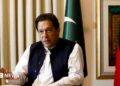 Former Pakistani Prime Minister Imran Khan speaks with Reuters during an interview, in Lahore, Pakistan March 17, 2023. He can be seen seated with his hand outstretched and speaking. Two Pakistani flags are behind him.