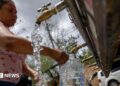 A woman fills a large container of water at a public tap