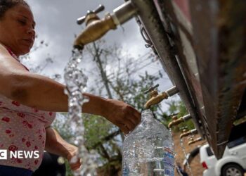 A woman fills a large container of water at a public tap
