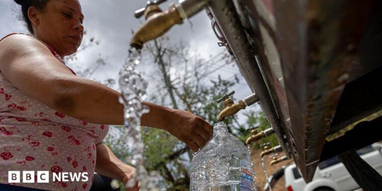 A woman fills a large container of water at a public tap