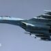 Image of a Russian Su-27, a whit and blue coloured fighter jet, airborne against a clear blue sky.