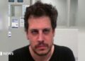 DHS released an mugshot of Yiannopoulos after his arrest. He wears a black shirt and has facial hair