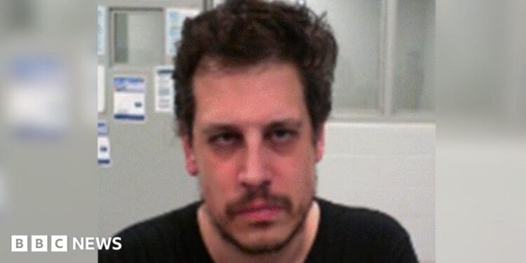 DHS released an mugshot of Yiannopoulos after his arrest. He wears a black shirt and has facial hair