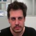 DHS released an mugshot of Yiannopoulos after his arrest. He wears a black shirt and has facial hair