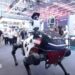 A humanoid robot riding a mechanical horse in front of onlookers