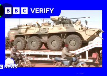 A Russian military vehicle being transported through the Malian capaitl, Bamako. Men on motorcycles are riding alongside it.