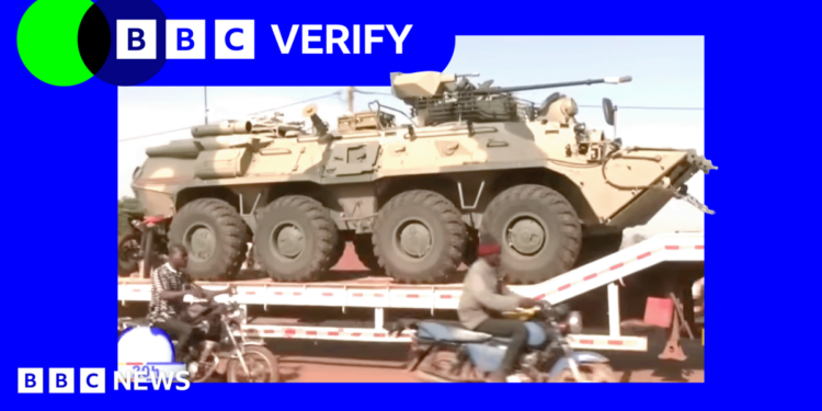 A Russian military vehicle being transported through the Malian capaitl, Bamako. Men on motorcycles are riding alongside it.