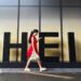 A woman in a red dress looks at her smartphone while walking past a Shein sign outside the company's office in Guangzhou, China.