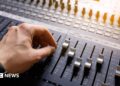A hand adjusting the knobs and faders on an audio mixer