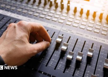 A hand adjusting the knobs and faders on an audio mixer