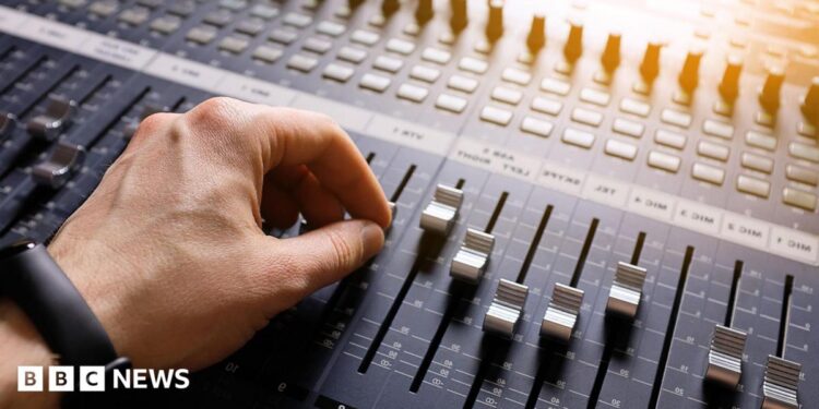 A hand adjusting the knobs and faders on an audio mixer