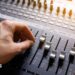 A hand adjusting the knobs and faders on an audio mixer