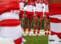 A pair of blurry legs in the foreground with a line of Sydney Swans players in the background